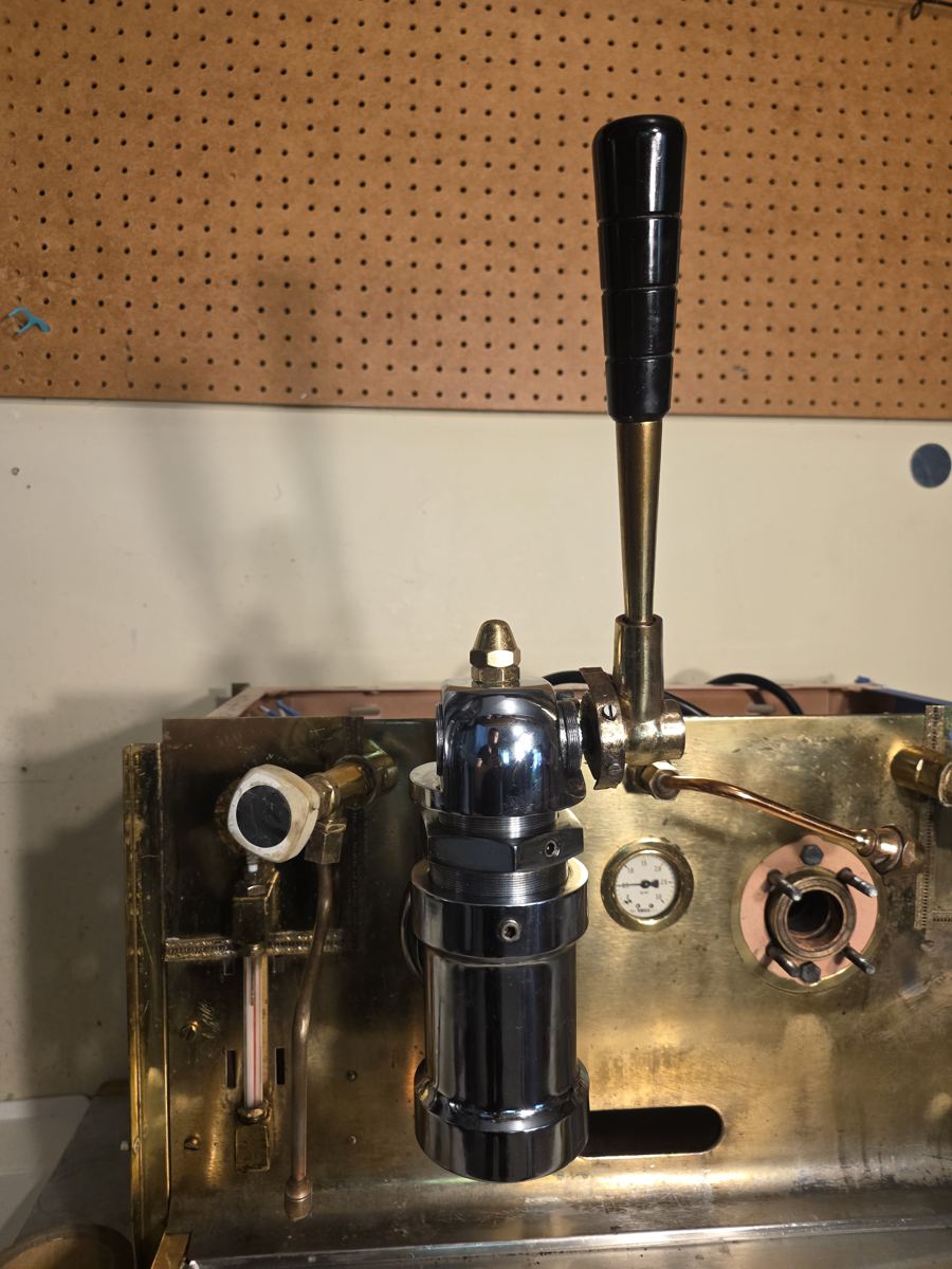 Chrome lever group head and pressure gauge on a brass espresso machine