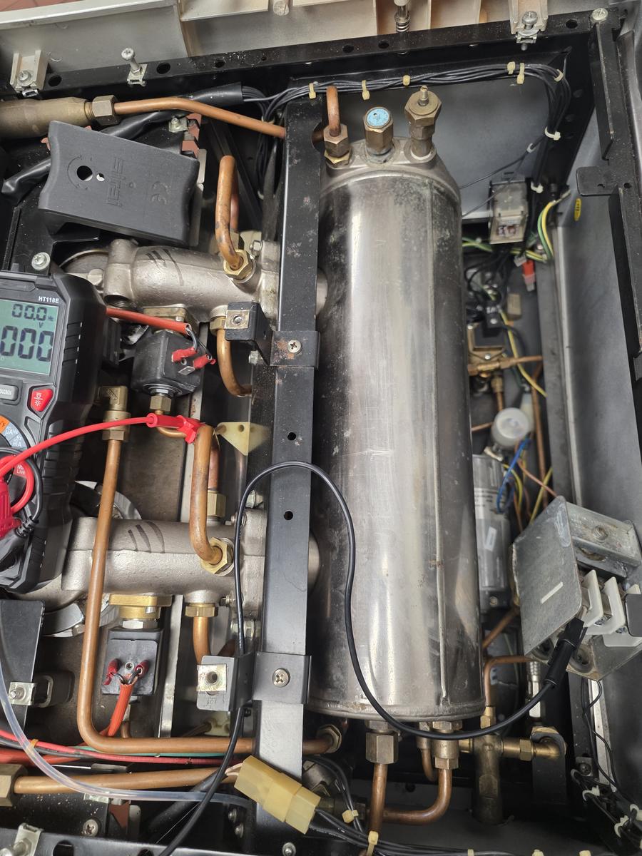 Inside a commercial espresso machine — boiler, solenoid valves and wiring being electrically tested with a multimeter by Amazigh Espresso